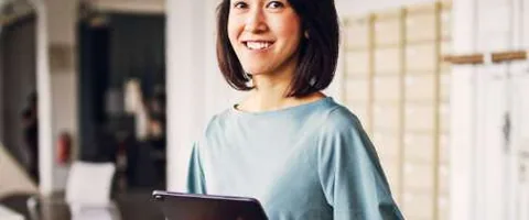 A woman smiles while holding a tablet.
