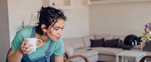 A woman using a laptop at home while holding a mug.