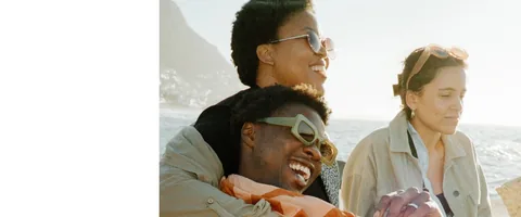 Three people sitting together beside the ocean.