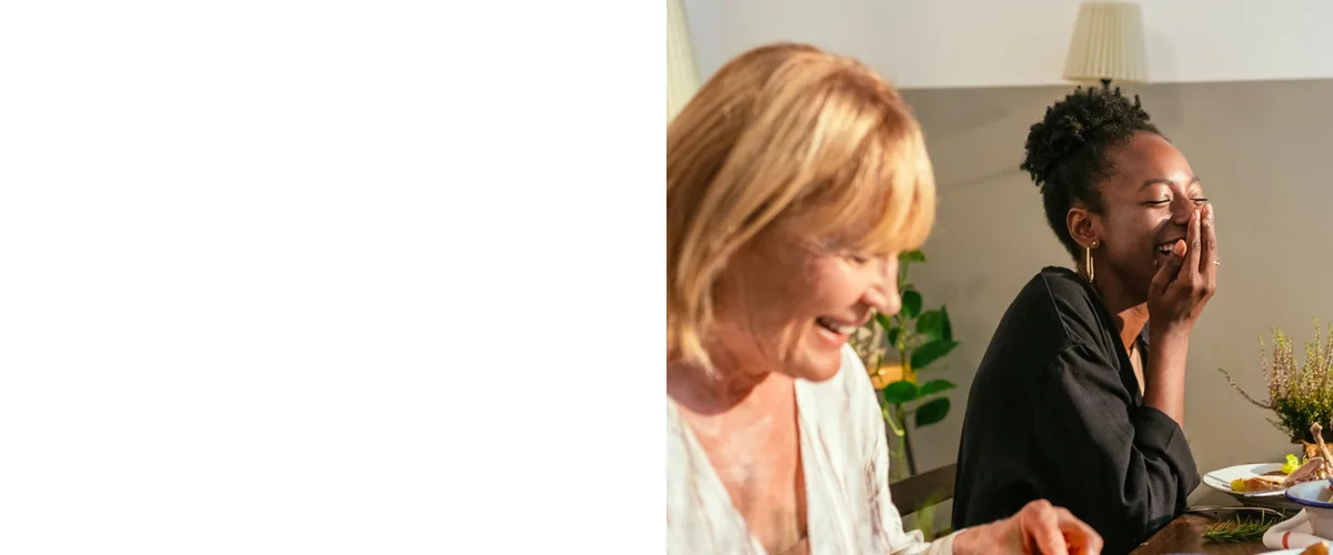 Three people laugh together over a meal at home.