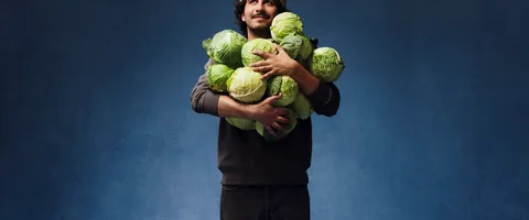 A person in a green knit cap holding an armful of cabbages.
