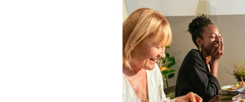 Three people laugh together over a meal at home.